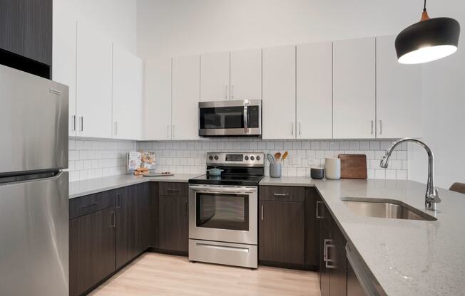 1 Bedroom Apartments In Wheat Ridge, CO - The Parallel - Gourmet Kitchen with White Upper Cabinets and Dark Brown Lower Cabinets, White Tile Backsplash, Quartz Countertops, Stainless Steel Appliances, and Luxury Plank Floors