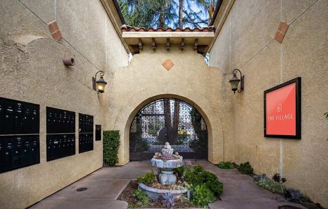 A stone archway leads to a courtyard with a fountain and a sign that says