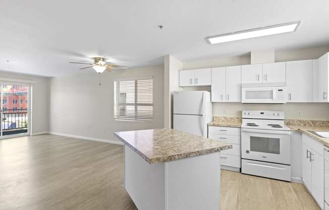 a kitchen with white cabinets and a white stove top oven with a view into the spacious living room with plank flooring at Promenade at the Park Apartment Homes, Washington