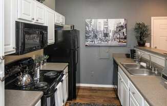 A black and white photo of a city street is hanging on the wall above a black refrigerator in a kitchen.