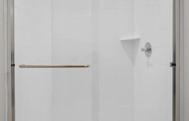 A white tiled shower with a glass door.