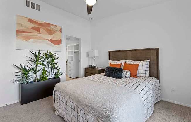 A bedroom with a bed, nightstand, and a plant.