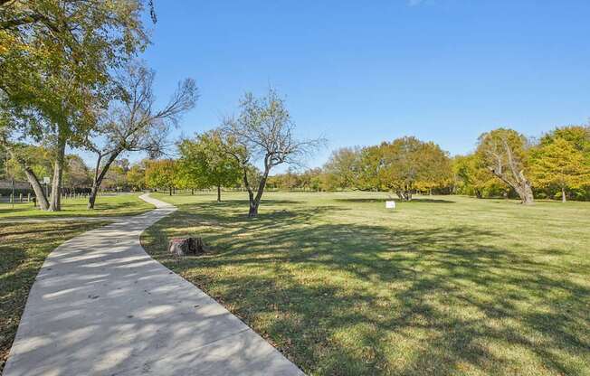 A concrete walkway leads through a grassy park with trees on either side.