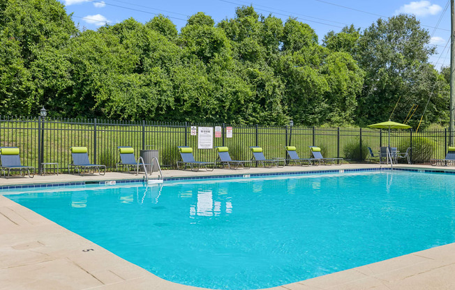 A pool surrounded by a fence with chairs and trees in the background.