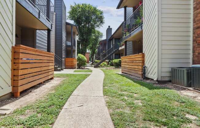 a path between two buildings with a wood fence on the left and a brick building on the