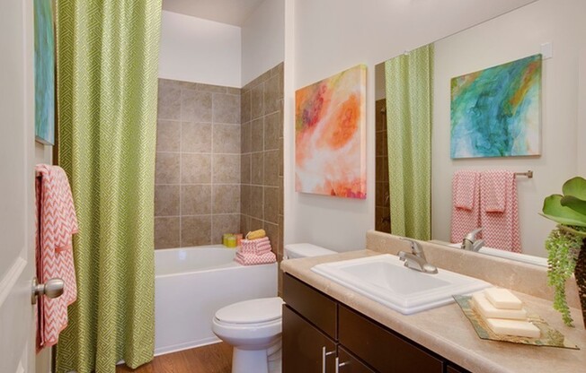 Photo of bathroom showing wood-style plank flooring, modern sink with modern cabinetry beneath, toilet, and bathtub with shower curtain.