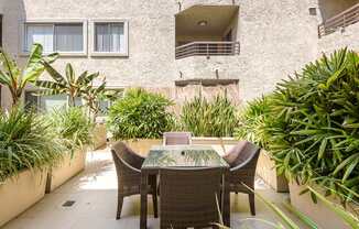 A patio with a table and chairs surrounded by green plants.