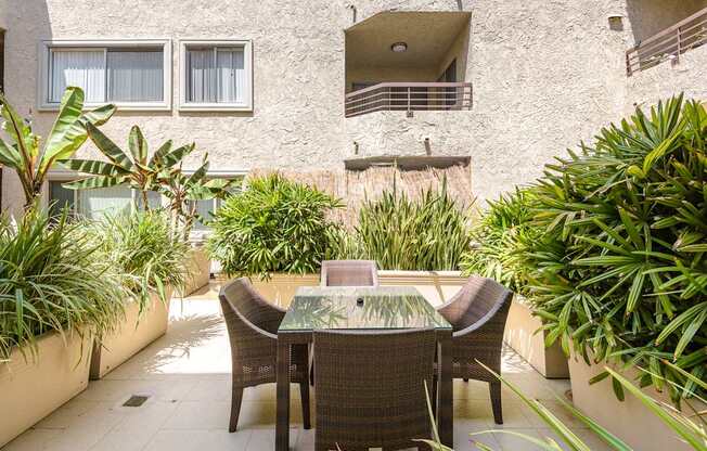 A patio with a table and chairs surrounded by green plants.
