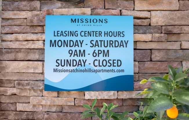 A sign on a brick wall that says "Missions Leasing Center Hours Monday - Saturday 9am - 6pm Sunday - Closed".