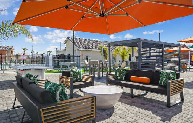 A patio with a table, chairs and a bench under an orange umbrella.