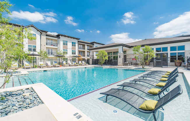 a swimming pool with lounge chairs in front of an apartment building