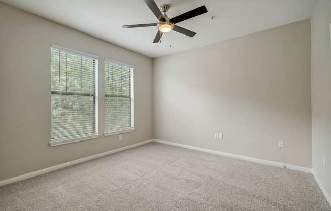 an empty living room with a ceiling fan and two windows