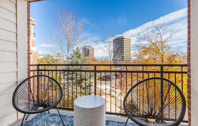 Two black chairs are placed on a balcony with a view of the city.