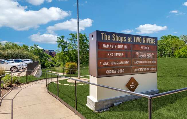 a sign for the shops at two rivers at the entrance to a park with cars