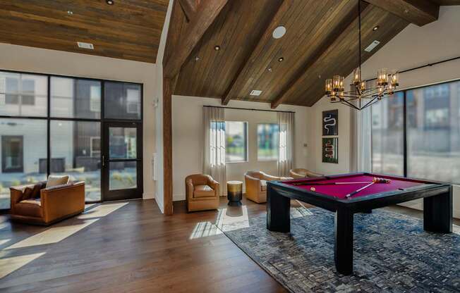 A pool table is in the middle of a room with a high ceiling and a lot of windows.