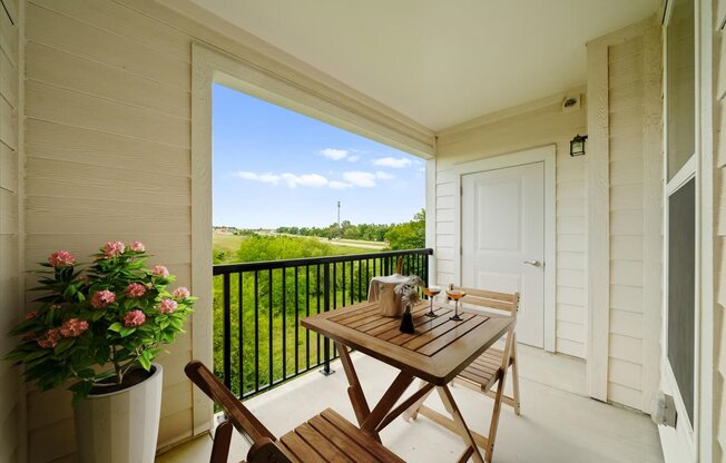 A balcony with a table and chairs overlooking a green landscape.
