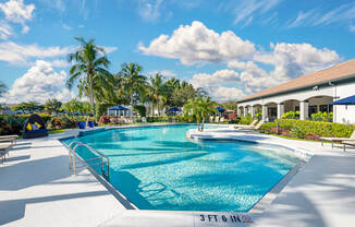 A large outdoor swimming pool with lounge chairs and an adjacent clubhouse overlooking a body of water