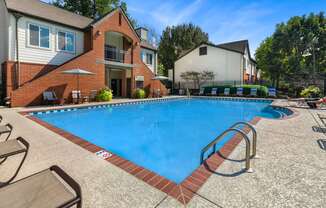 A swimming pool surrounded by a brick border and lounge chairs.