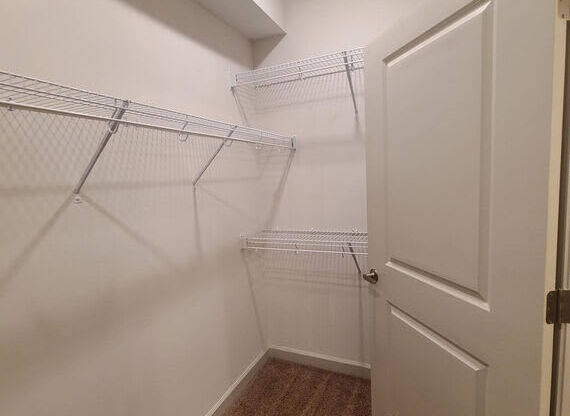 A white door is on the right side of a hallway with a carpeted floor and a metal rack on the wall.