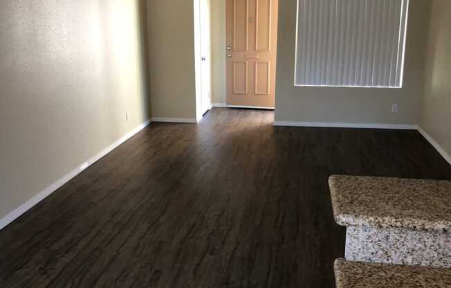 Kitchen view of living room and front enterance with large window for great natural light at Plaza Verde Apartments in Escondido, California.