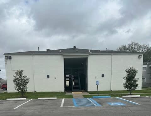 A white building with a grey roof and a parking lot in front.