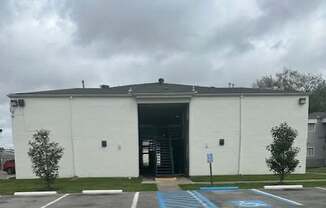 A white building with a grey roof and a parking lot in front.