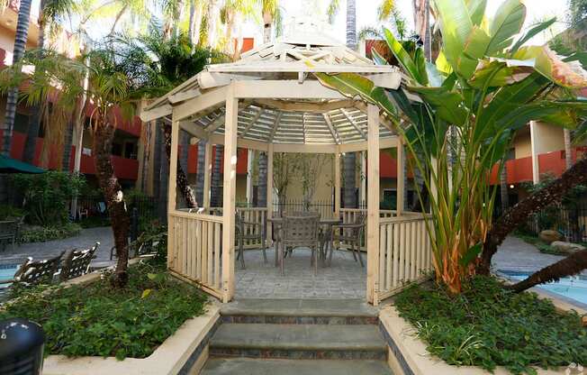 A gazebo with a table and chairs is surrounded by plants.