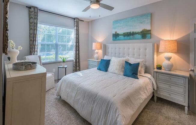 Furnished bedroom with queen size bed, two night stands, large windows, ceiling fan, high ceiling and carpet flooring at Evergreens at Mahan in Tallahassee, FL