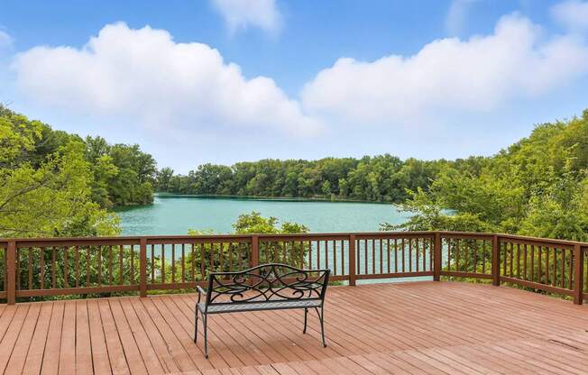 A bench sits on a wooden deck overlooking a lake.