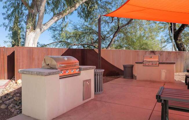 A patio with a grill and an orange umbrella.