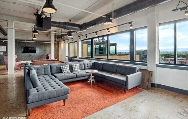 A grey couch with a pillow is in the middle of a room with a red carpet at Archer Tower in Denver, CO