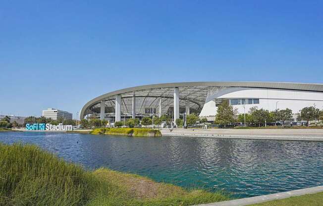 A modern stadium with a curved roof and a body of water in front.
