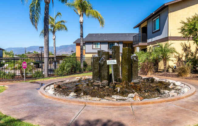 A small fountain in the middle of a circular walkway with a sign in front of a building.