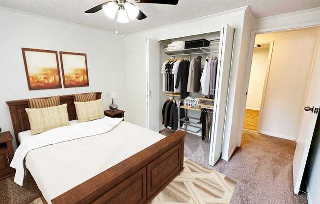 A bedroom with a large bed and a closet with clothes hanging.