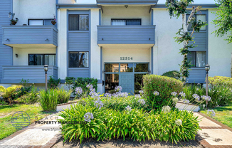 an apartment building with blue and white siding and a flower garden in front of it