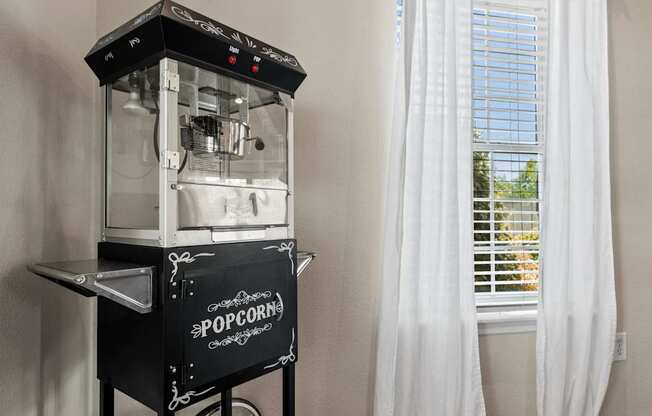 A popcorn machine sits on a table next to a window.