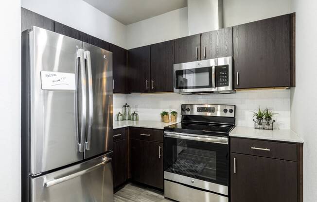 Kitchen with dark cabiets, stainless steel appliances, quartz countertops, and subway tile backsplash