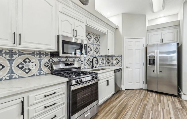 A kitchen with white cabinets and a black and white tiled backsplash.