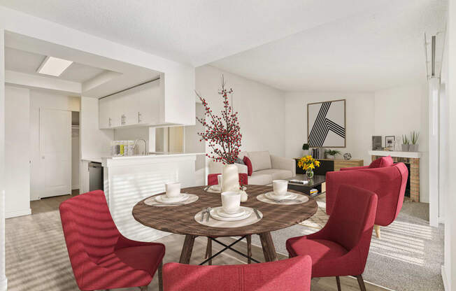 Dining area with white walls and the kitchen is to the left, and the living room is to the right. Staged with a round table and 4 red chairs.