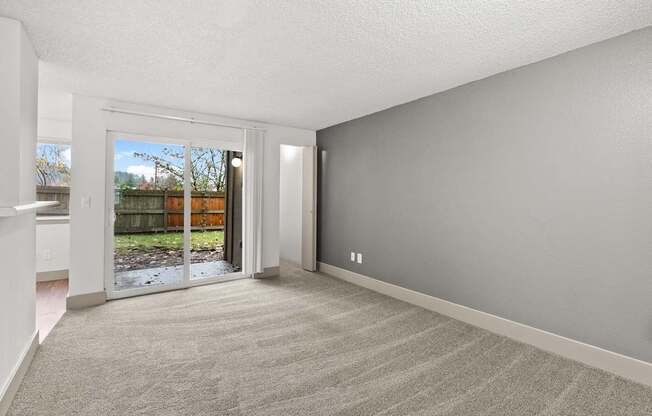 A room with a carpeted floor and a sliding glass door leading to a backyard.