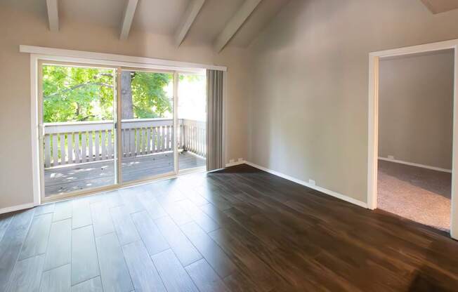 A room with wooden floors and a sliding glass door leading to a balcony.