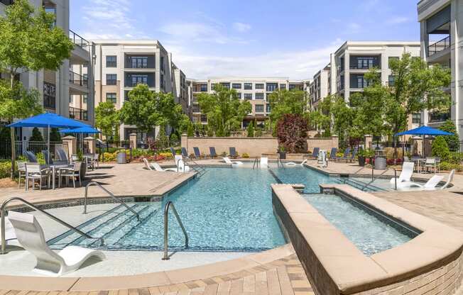 a swimming pool with lounge chairs and umbrellas in front of an apartment building