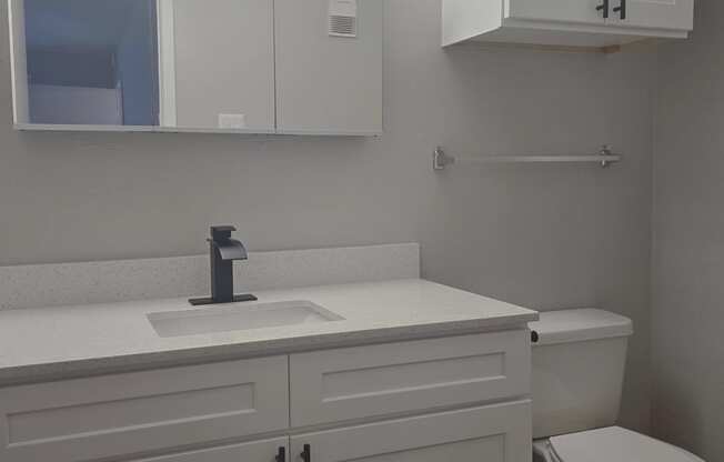 a bathroom with white cabinets and a toilet and sink