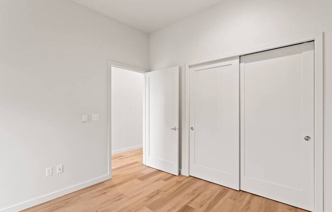 A white room with a wooden floor and three white doors.