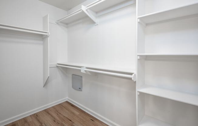 a walk in closet with white shelves and a wood floor