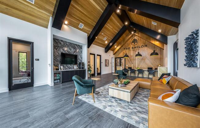 A clubhouse lobby with a lounge, meeting table, and beverage station at The Shiloh Apartments.
