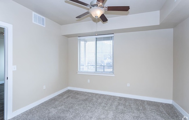 A room with a ceiling fan and a window with blinds.