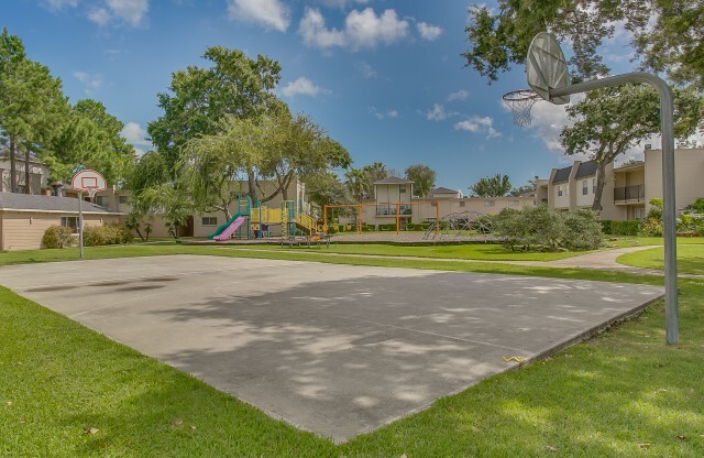 View of Basketball Court, Showing Basketball Hoops, Grass, and Playground in Background at The Regatta Apartments