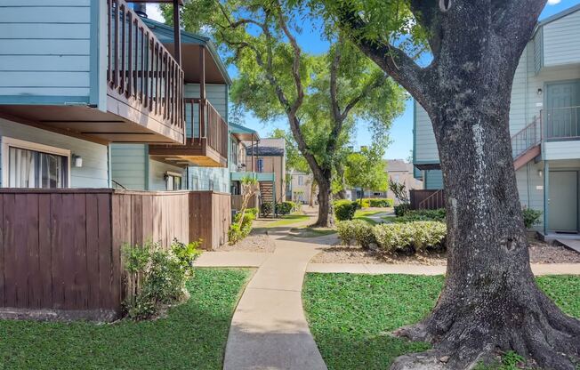 a pathway between two apartment buildings with trees and grass