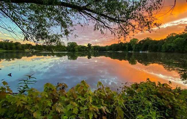 A serene lake surrounded by lush greenery under a vibrant sunset.